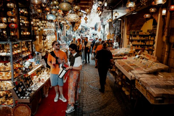 A bustling scene in İstanbul's Grand Bazaar with colorful lamps, shoppers, and vibrant market stalls.