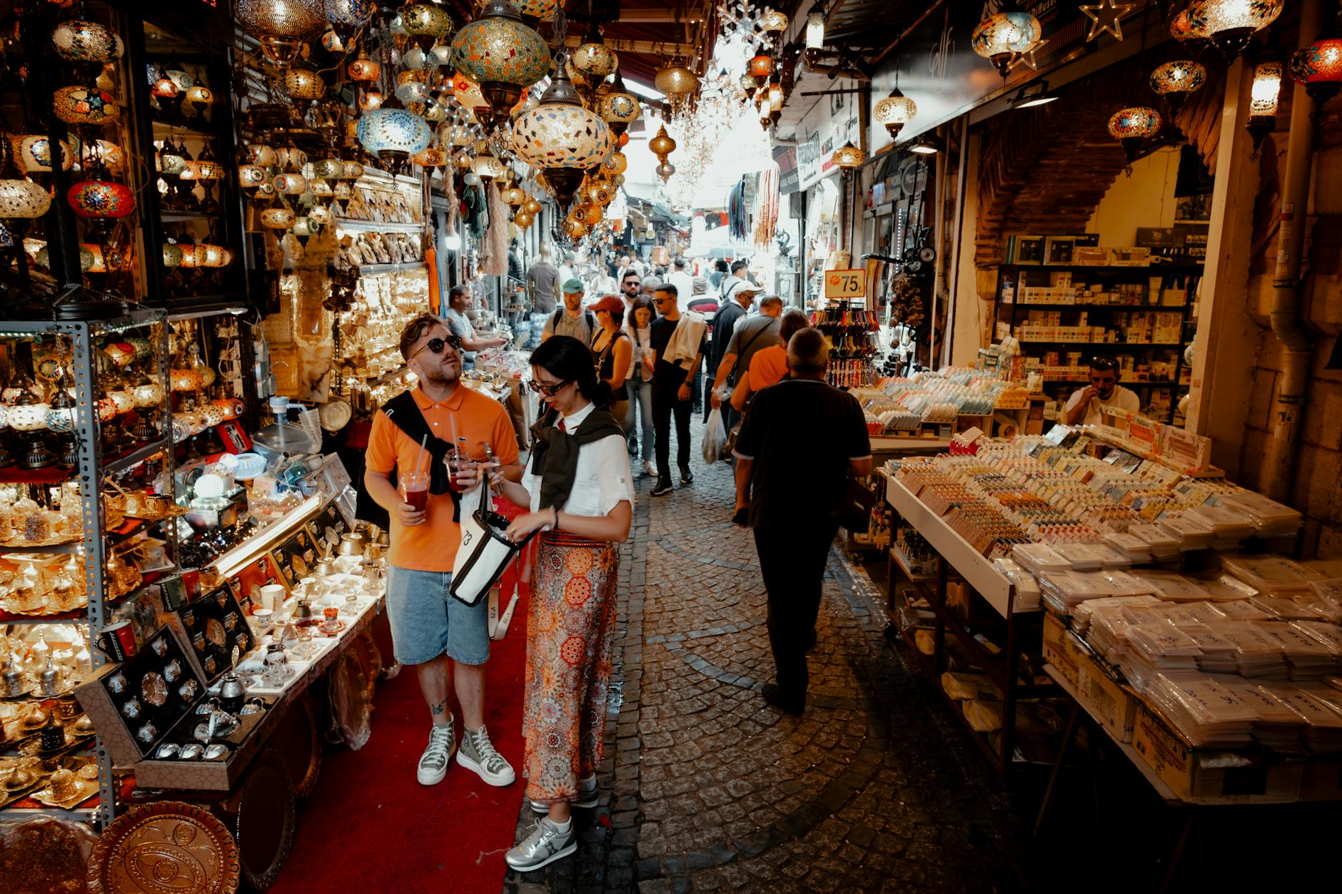 A bustling scene in İstanbul's Grand Bazaar with colorful lamps, shoppers, and vibrant market stalls.